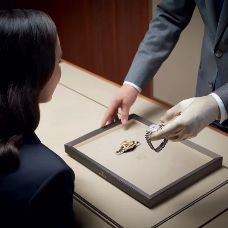 Rolex sales associate showcasing a Rolex watch on a presentation tray to a seated client.
