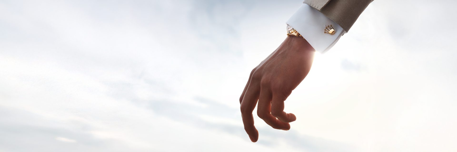 Close-up of gold Rolex Crown cufflinks worn on a shirt cuff alongside a Rolex watch.