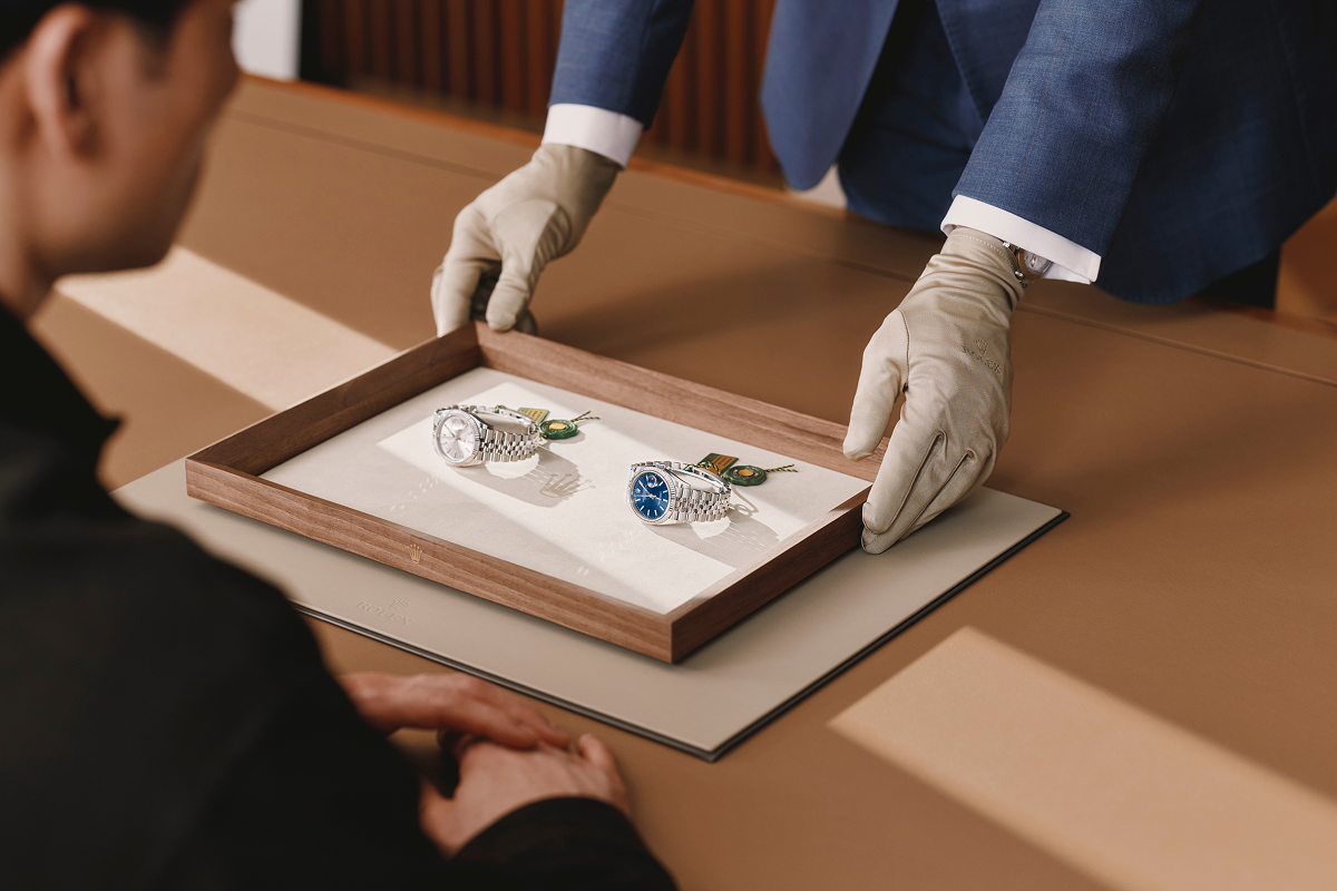 Rolex sales associate presenting two Rolex Datejust watches on a tray to a customer.