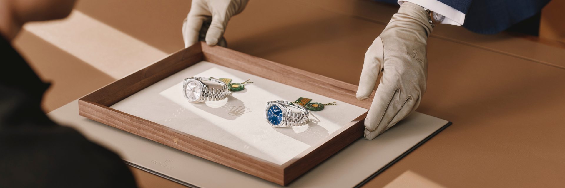 Rolex sales associate presenting two Rolex Datejust watches on a tray to a customer.